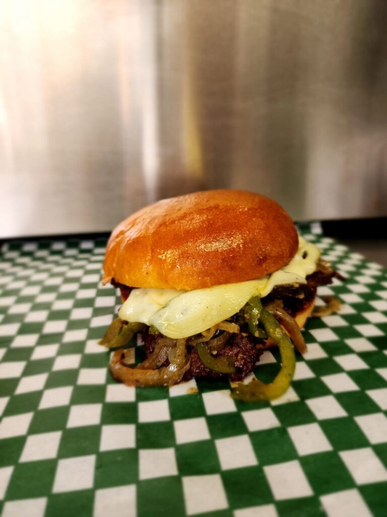 Burger with melted cheese, grilled peppers, and onions from Smashed YXY